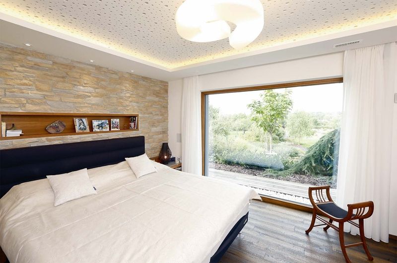 Ložnice s výhledem do zahrady a protihlukovou deskou na stropě, která ladí s designovým svítidlem.