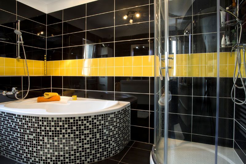 Na koupelně v černo-žluto-bílém pojetí se nezávisle na sobě shodli pán i paní domu. Černé velkoformátové obklady umožňují těm žlutým pěkně zazářit.
