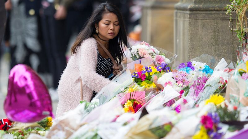 Žena před manchesterskou radnicí pokládá květiny za oběti. 
