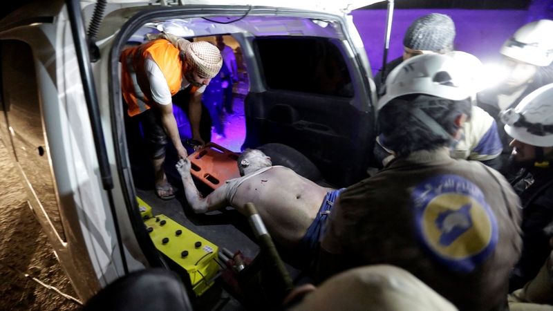 Příslušník civilní obrany nakládá zraněného po náletu na Idlíb.