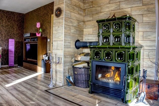 Hezkým prvkem zařízení interiéru obývacího pokoje s jídelnou jsou lahvově zelená kachlová kamna.