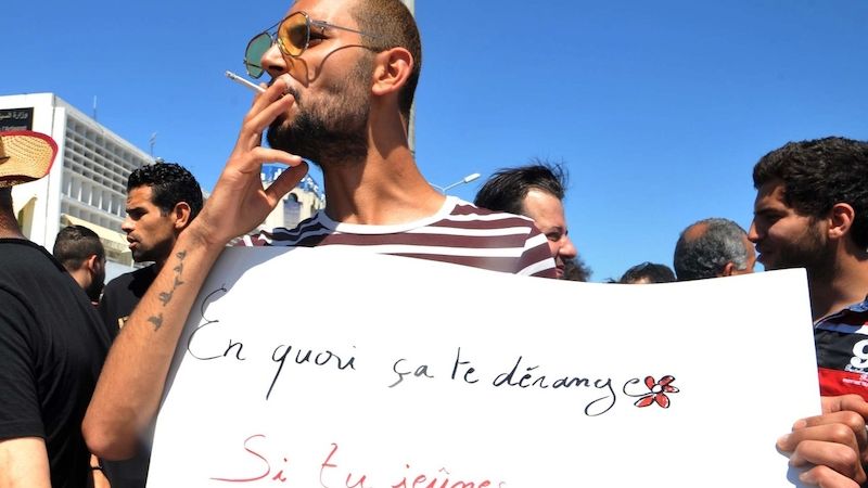 Tunisané protestují proti trestání lidí, kteří se během ramadánu nepostí. Ostentativně kouřící muž nese transparent s nápisem ve francouzštině: Proč ti vadí, že se postíš a já jím?
