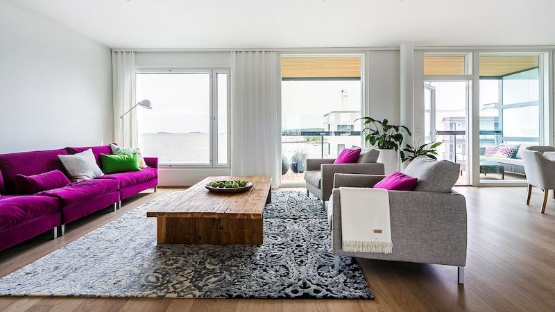 Obývací pokoj je vybavený pohovkou Donna ve fuchsiové barvě doplněnou šedými křesly stejné značky. Teakový stůl stojí na šedém koberci od Designer’s Guild. 