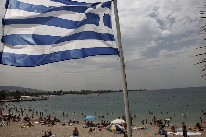 Řecká vlajka u zalidněné pláže na předměstí Atén.