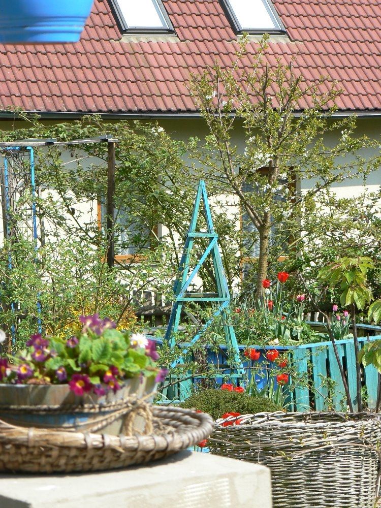 V užitkové zahradě je čtveřice vyvýšených záhonů vyrobená z modře natřených palet a mezi nimi je čtyřboký jehlan.