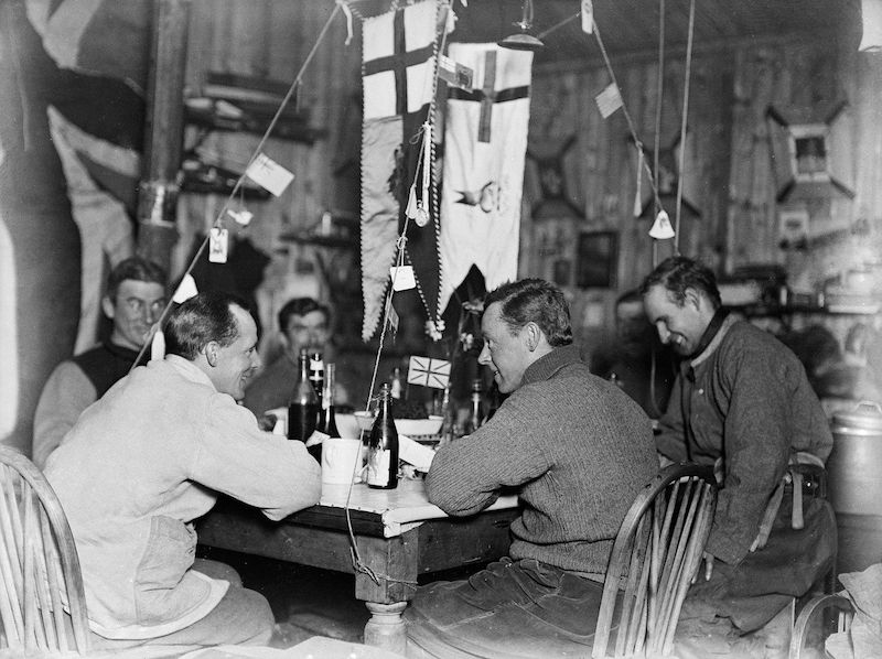 Členové severního týmu oslavují polovinu zimy 22. července 1911 v chatě u mysu Adare.