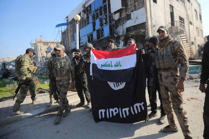 Příslušníci iráckých bezpečnostních sil drží iráckou vlajku i strženou vlajku Islámského státu, kterou strhly ze sídla provinční vlády v Ramádí.  