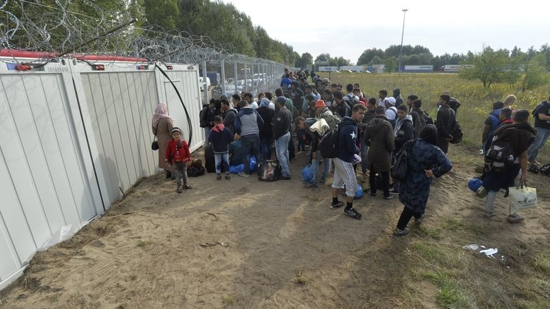 Migranti čekají u kontejnerů, kde úředníci vyřizují jejich žádosti o azyl.