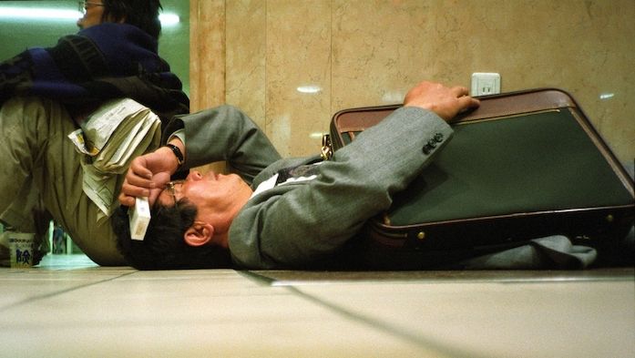 Vyčerpaný japonský finančník odpočívá na vlakové stanici.