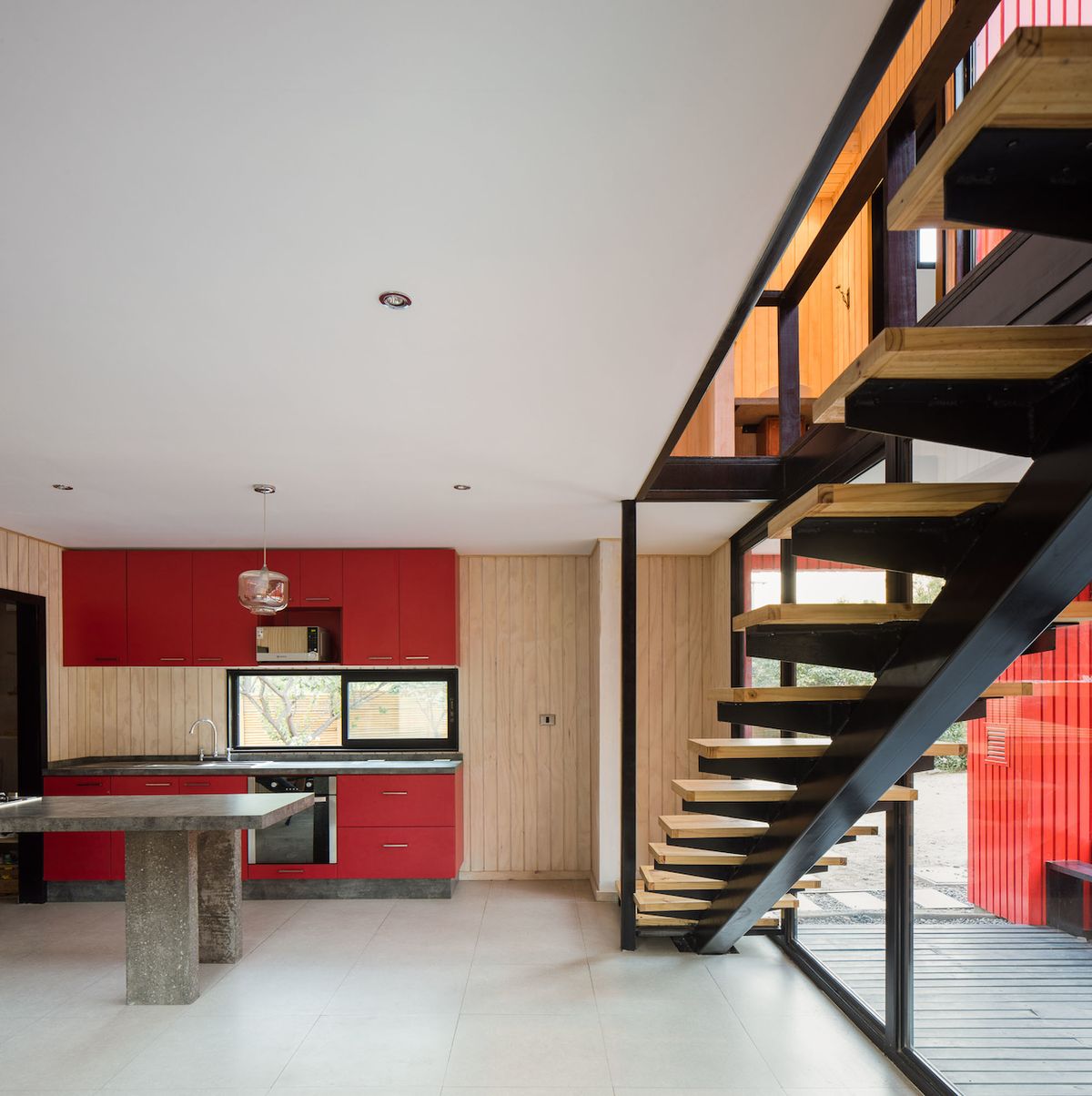 Zatímco dřevěné obklady z fasády se objevují v interiéru domu v přírodní barvě, linka v kuchyni opakuje barvu červenou.