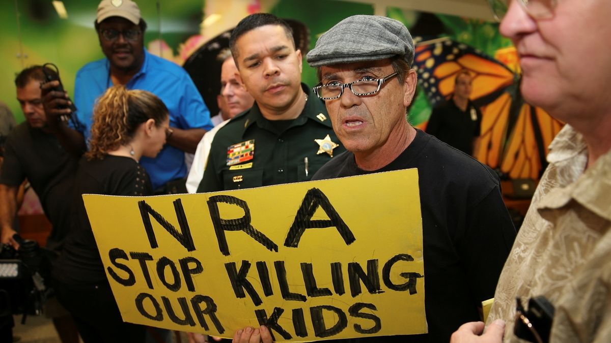 Lidé před soudem, kde stanul útočník z floridské střední školy Nikolas Cruz, protestují proti vlivné organizaci NRA, která zastupuje zájmy výrobců zbraní a hájí jejich volný prodej. Cruz poloautomatickou pušku AR-15 koupil legálně.
