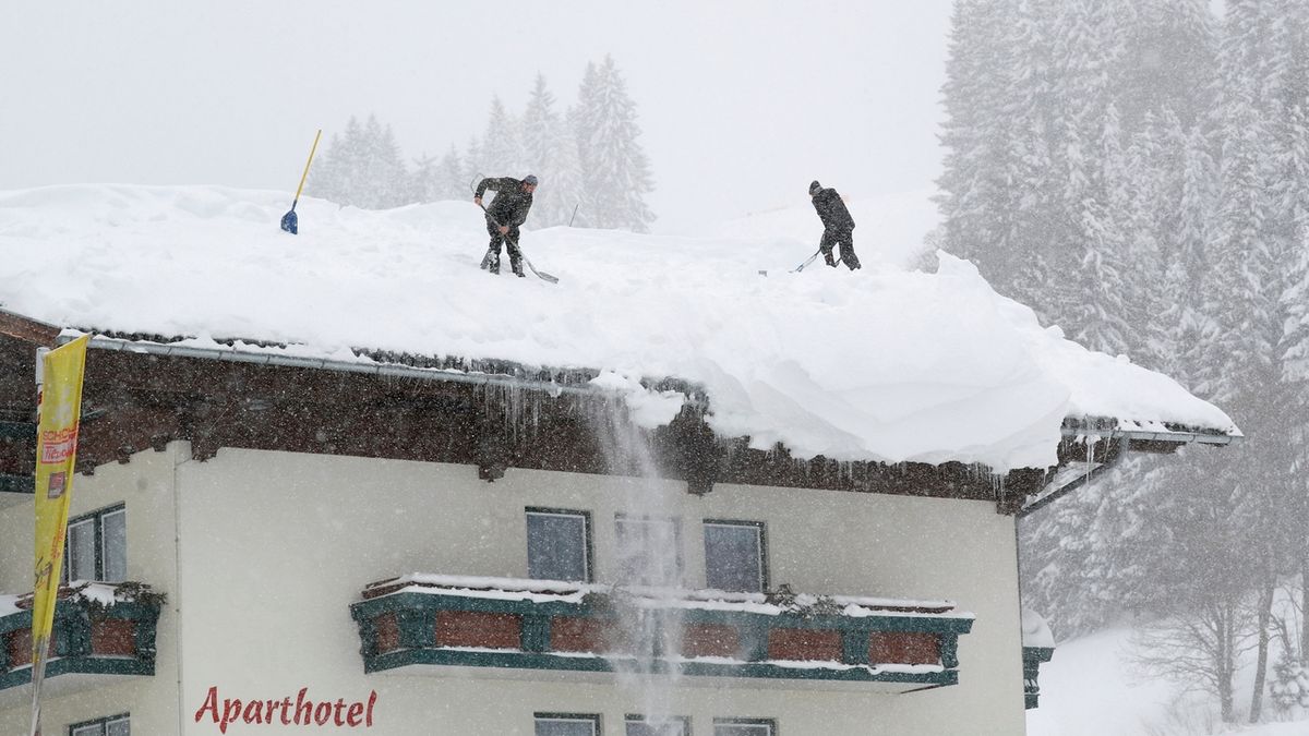 Dva Rakušané shazují sníh ze střechy domu  v Filzmoosu. 