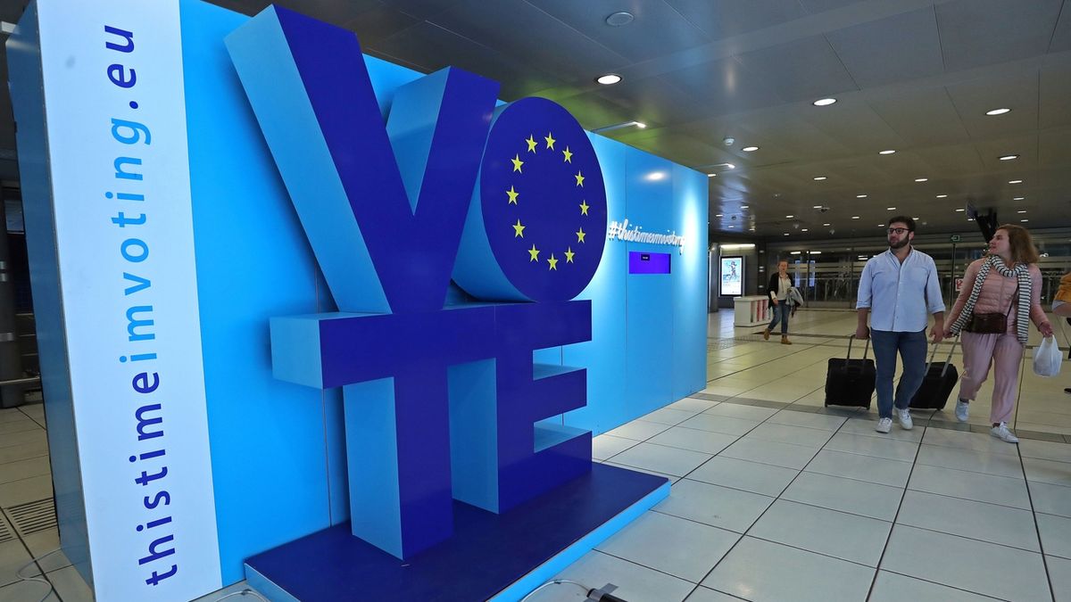 Cestující u bruselského sídla Evropského parlamentu procházejí kolem reklamního plakátu, vyzývajícího k účasti v eurovolbách.