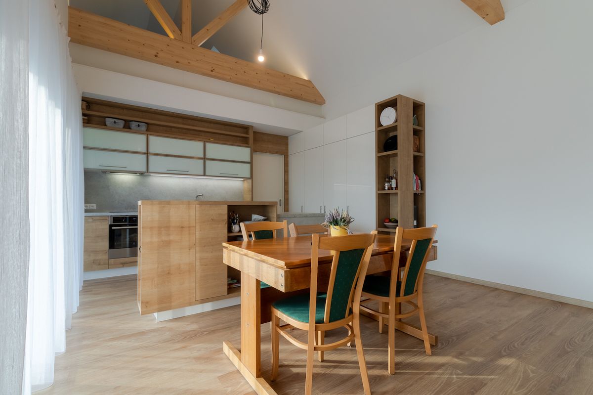 Úložné prostory v kuchyňské části jsou v nápadité kombinaci bílého lesku a přírodního dřeva.