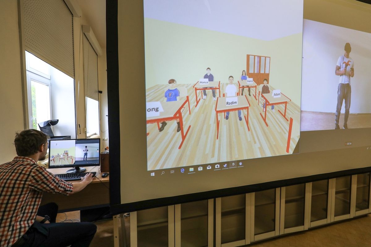 Za projekčním plátnem je student s 3D brýlemi, v druhé části třídy sledují jeho výkon spolužáci a vyučující.