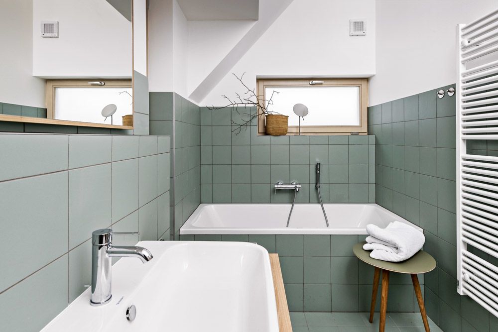 V koupelnách byly záměrně vybrány zelenkavé obklady, které se v matné povrchové úpravě vhodně doplňují s povrchy smrkového a dubového dřeva a působí jednoduše a nadčasově.
