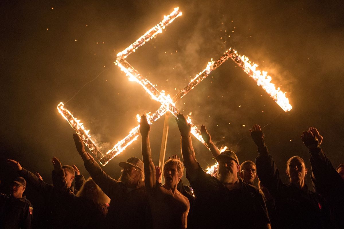 Přiznivci National Socialist Movement, nacionalistické politické organizace pouze pro bílé, hajlují během pálení svastiky na nespecifikovaném místě ve státě Georgia v USA.