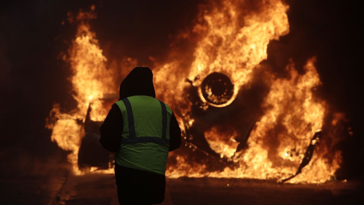 Demonstrant sleduje hořící vůz u Champs-Elysees při protestech, které probíhaly 1.12. v Paříži.