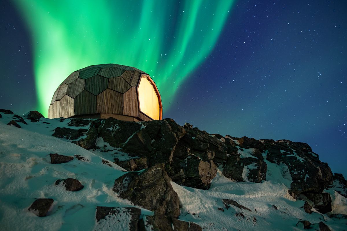 Velké okno chatky nabízí úchvatné výhledy do okolní polární krajiny přes den. V noci je ovšem zastiňuje polární záře.