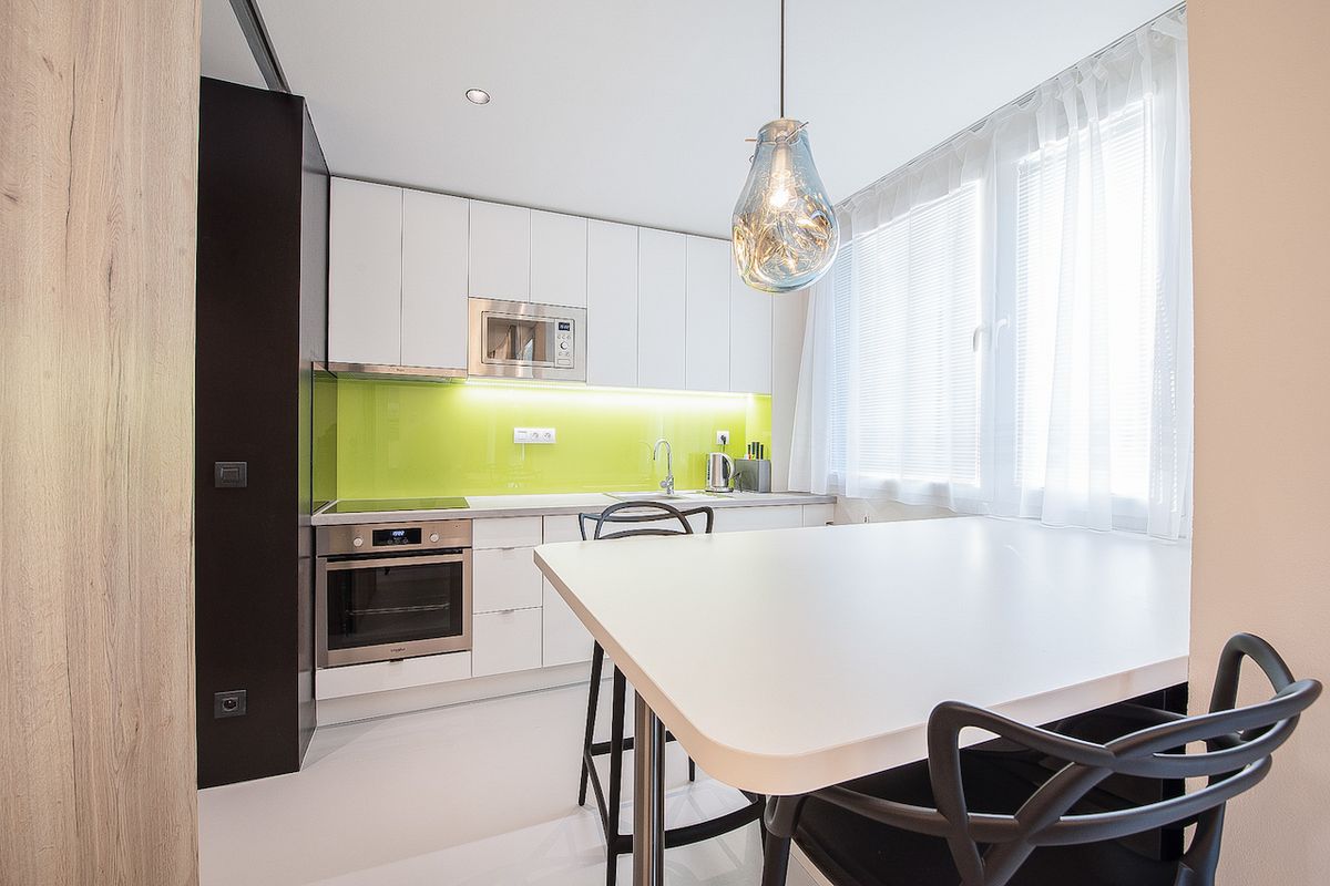 Kuchyňský kout je ozvláštněn světle zeleným pruhem na zádech linky a zajímavě tvarovanými židlemi u jídelního stolu.