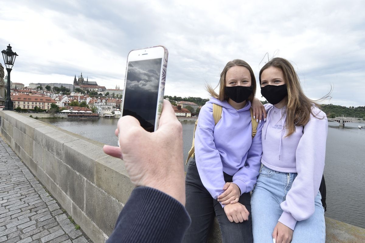 Dívky s rouškami na obličejích se fotografují 24. května 2020 na Karlově mostě v Praze.
