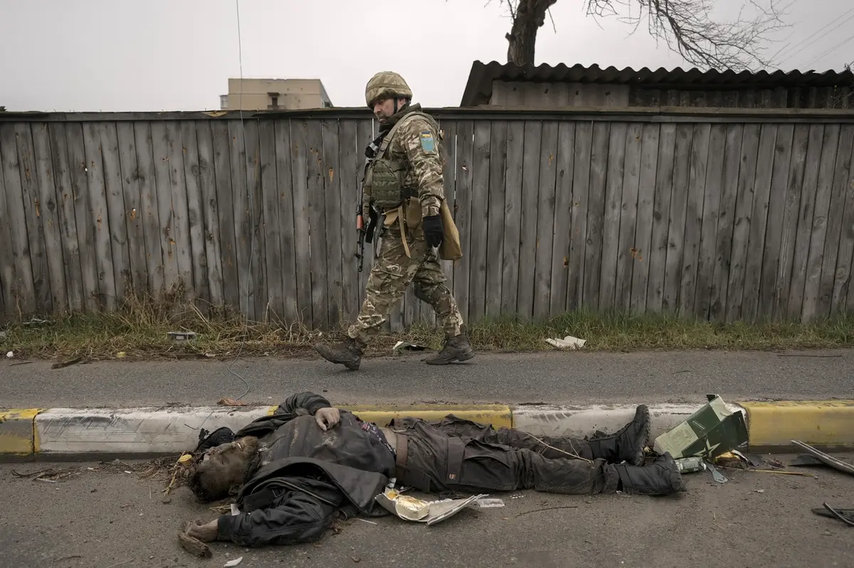 Ukrajinský voják u těla mrtvého civilisty v Buči.