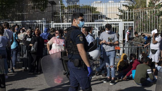 Řecký policista a migranti před azylovým centrem v Aténách.
