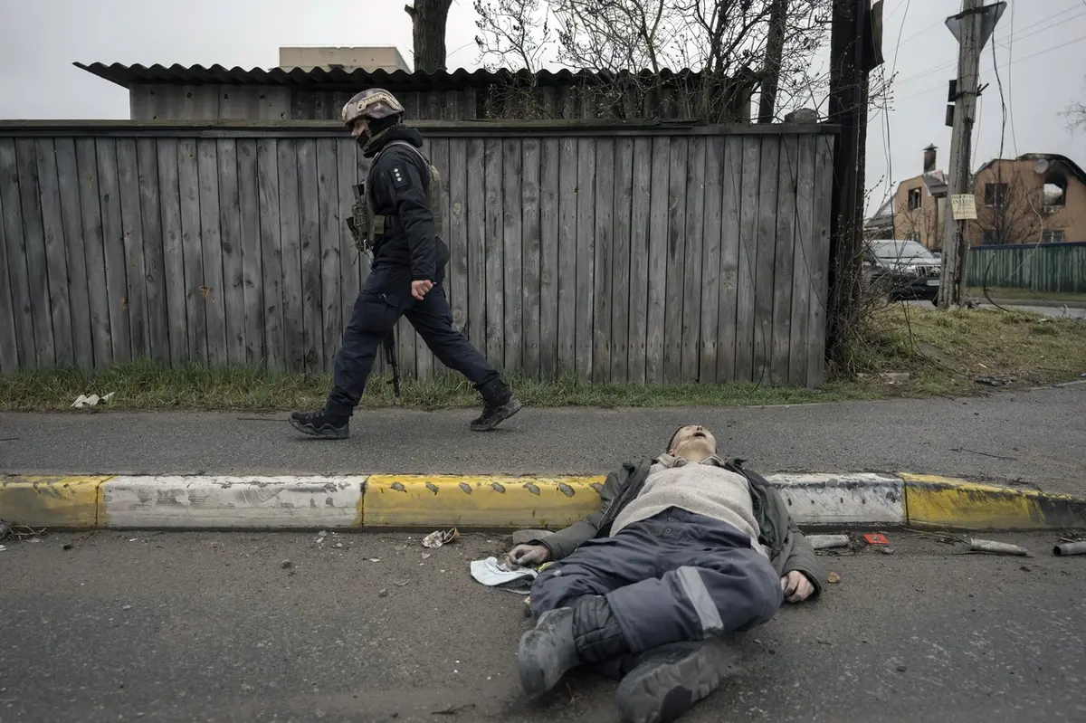 Ukrajinský voják prochází kolem mrtvého civilisty na ulici v Buči.