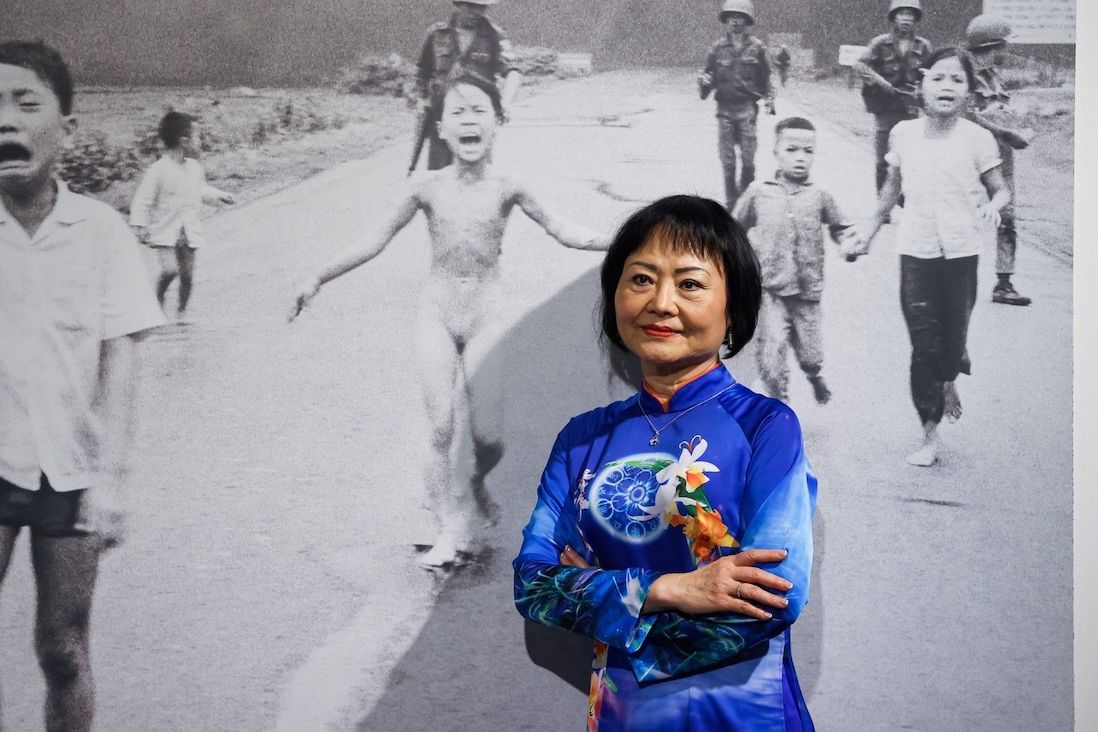Kim Phuc v pozadí se snímkem, kde jako devítiletá utíká s popáleninami po napalmu