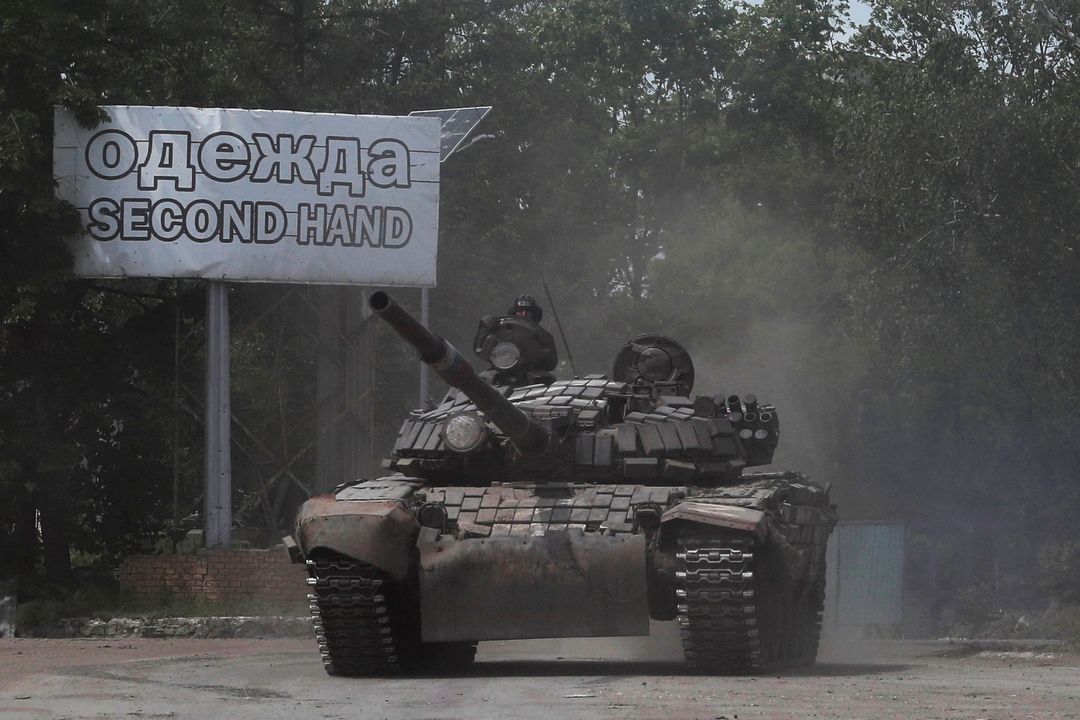 Tank proruský separatistů v Popasné míjí tabuli upozorňující na bazar s oblečením. 