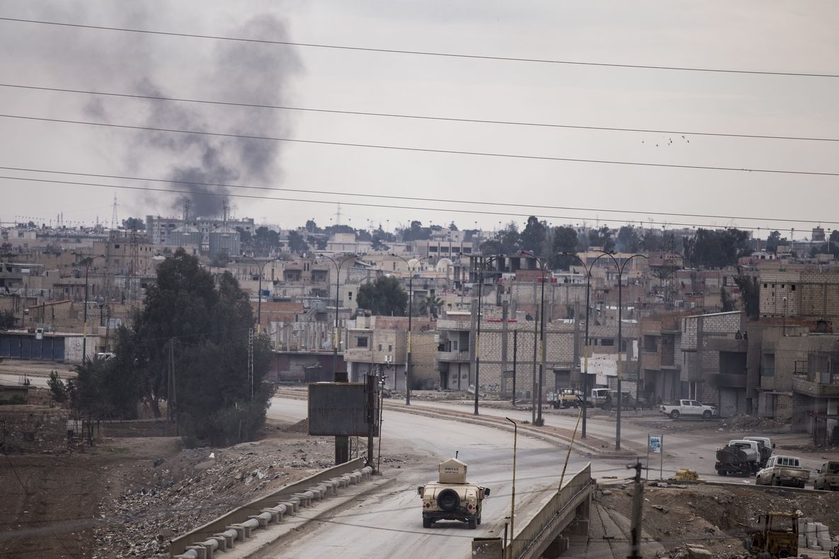 Bojovníci kurdské milic SDF hlídkují v humvee v Hasace, nad kterou stoupá dým 