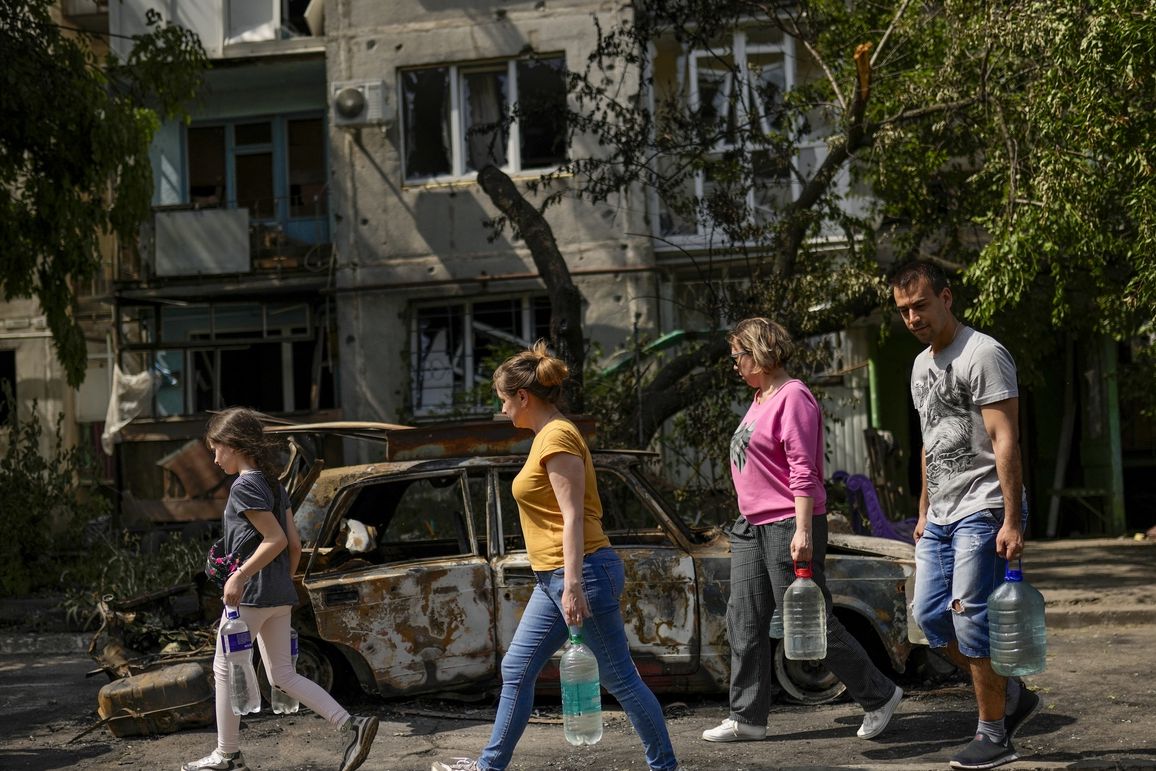 Местные жители несут воду рядом со зданием, поврежденным в результате ночного ракетного обстрела в Славянске