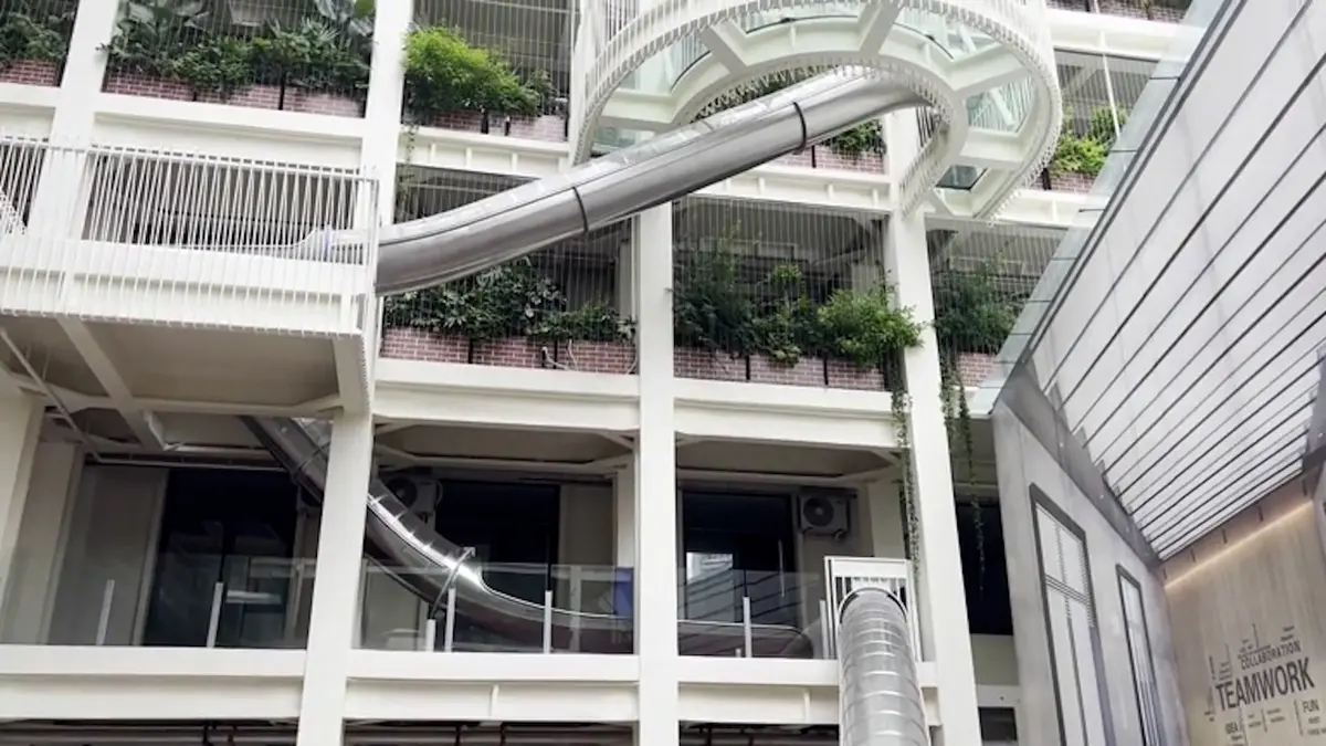 The facade of the office building is covered with greenery and crossed by slides for employees