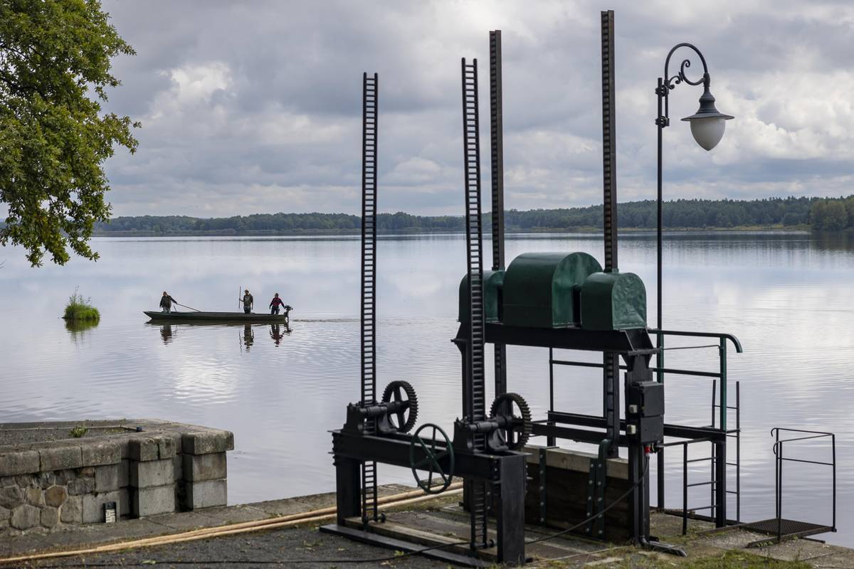 Rybáři hlídají hladinu rybníka a zbavují ji nečistot.