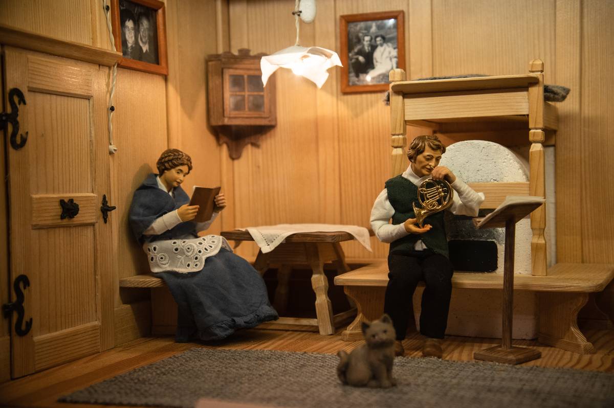 Scéna zobrazuje tradiční tyrolskou světnici, v originále „stube“.