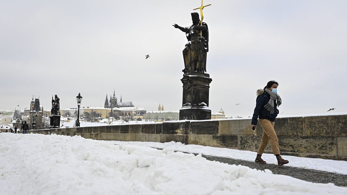 Žena v roušce proti šíření koronaviru prochází 8. února 2021 po zasněženém Karlově mostě v Praze.