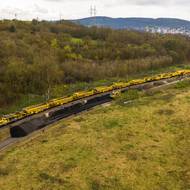 Pohled z výšky na železniční trať kousek za Berounem (na snímku v pozadí). Na trati projíždí sanační stroj AHM 800R, který přes Velikonoce obnovoval železniční svršek a spodní stavbu mezi Karlštejnem a Srbskem. Odtěžuje starý materiál, který skládá na jednotlivé vagony, a zároveň ho nahrazuje materiálem novým.