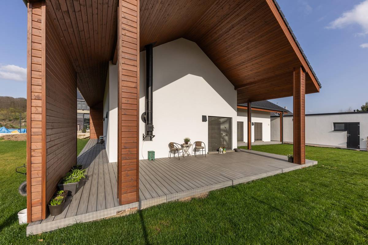 Přetažením střechy vznikla prostorná krytá terasa. Strana směřující do ulice je plná, vzniklo tak příjemné místo k posezení.