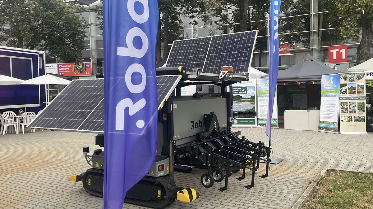 Farmář u mobilu. Na poli jsou roboti, po louce se potuluje kurník na solární pohon