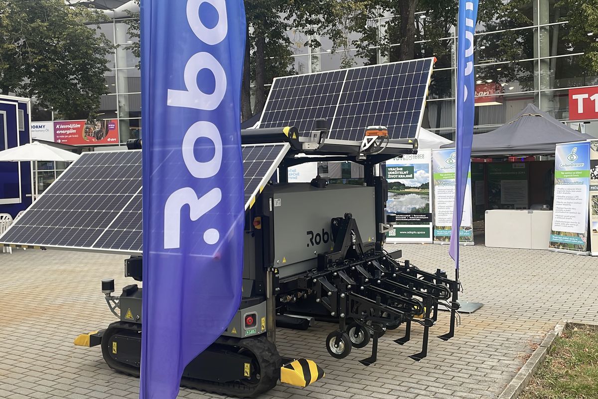 Farmář u mobilu. Na poli jsou roboti, po louce se potuluje kurník na solární pohon