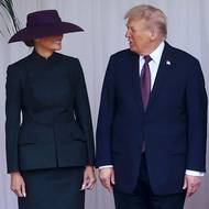 Melania zvolila černý kostým a fialový klobouk s širokou krempou.