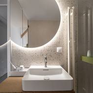 Koupelna v půdním bytě pracuje s tmavě mořeným dřevem. Podsvícení zrcadla navozuje intimní atmosféru pro příjemné sprchování. 