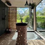 Koupelnu s vestavnou vanou propojují s venkovní přírodou velká bezrámová okna. Podstavec pro umyvadlo vytvořil na míru sochař Michal Trpák.