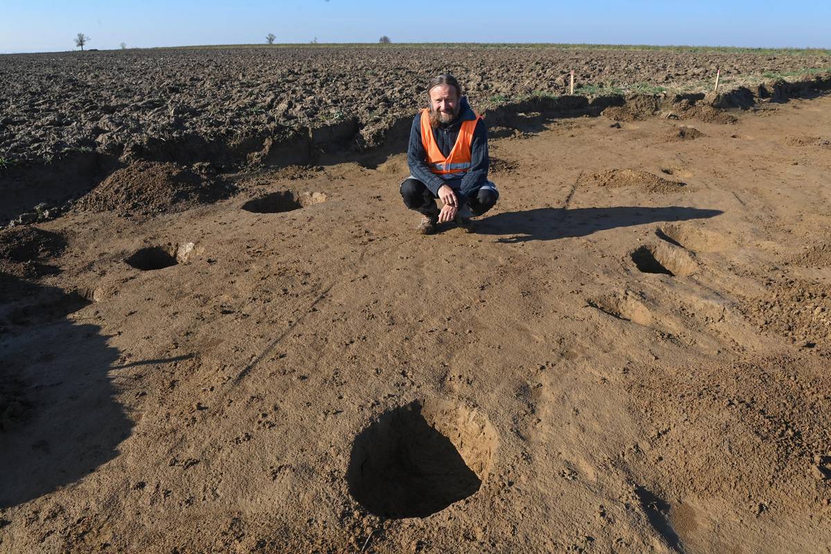 Vedoucí výzkumu Marek Kalábek ukazuje několik jamek, ve kterých byly původně zasazené nosné kůly pravěkého obydlí.
