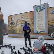 Otec se synem krmí holuby v centru Dobropillja u sochy ukrajinského národního hrdiny Tarase Ševčenka. 15.února 2025.