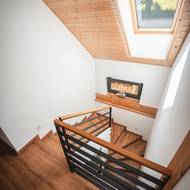 Schodiště působí vzdušně díky střešnímu oknu, které přivádí dostatek denního světla. Dřevěné obložení a černé zábradlí vytvářejí příjemný kontrast.