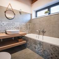 Koupelna je laděná do šedých odstínů, které doplňují výrazné dekory na obkladech. Díky nim působí interiér útulně a originálně.