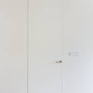 Bílé vysoké dveře bez obložek jsou ve stěně takřka neviditelné.