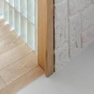 Detail kontaktu luxferové stěny, stěrky a dubové podlahy v průchodu z obýváku do ložnice.