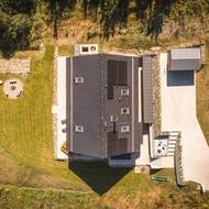 Pohled shora ukazuje promyšlený celek. Moderní dřevostavba, terasa, ohniště i dřevník tvoří harmonické propojení domu s přírodou.